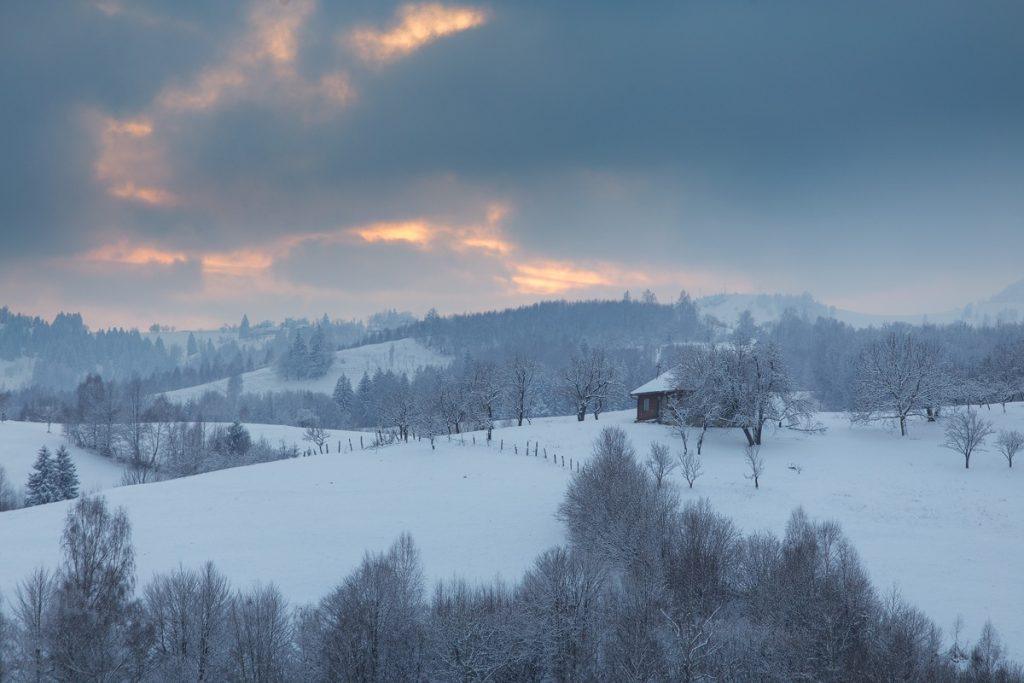 fotografie de peisaj de iarna la apus cu ninsoare in satul pestera brasov